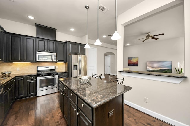 kitchen featuring a breakfast bar, appliances with stainless steel finishes, dark stone countertops, decorative backsplash, and decorative light fixtures