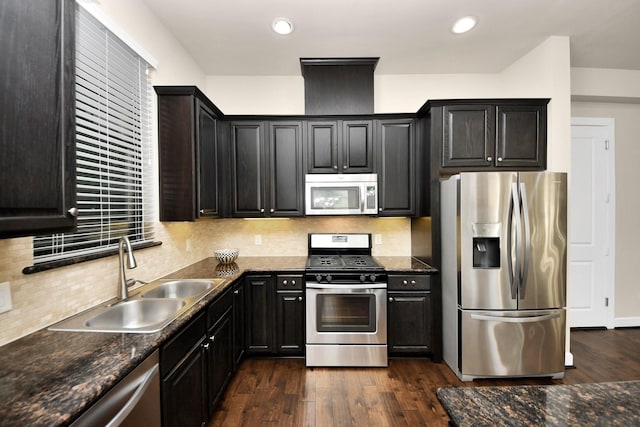 kitchen featuring appliances with stainless steel finishes, sink, dark stone countertops, dark hardwood / wood-style flooring, and decorative backsplash