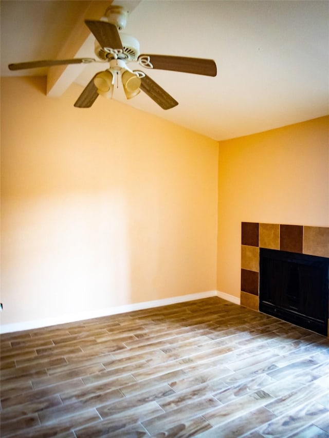 empty room featuring hardwood / wood-style flooring, vaulted ceiling, a tile fireplace, and ceiling fan