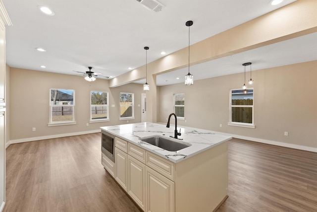 kitchen with hardwood / wood-style floors, pendant lighting, an island with sink, sink, and light stone countertops