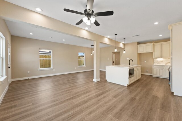 kitchen with sink, decorative light fixtures, light wood-type flooring, an island with sink, and backsplash