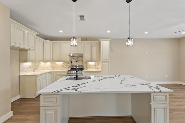 kitchen featuring light stone countertops, a kitchen island with sink, stainless steel range with gas cooktop, and decorative light fixtures