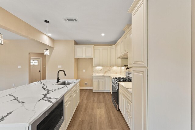 kitchen with appliances with stainless steel finishes, sink, decorative backsplash, hanging light fixtures, and light stone counters