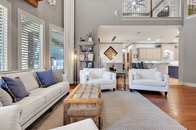 living area featuring baseboards, a towering ceiling, an inviting chandelier, crown molding, and light wood-type flooring