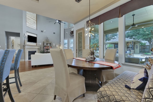 dining space with light tile patterned floors, a healthy amount of sunlight, a fireplace, and ceiling fan with notable chandelier