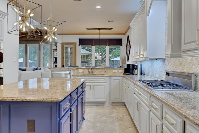 kitchen with appliances with stainless steel finishes, ornamental molding, blue cabinets, an inviting chandelier, and white cabinetry