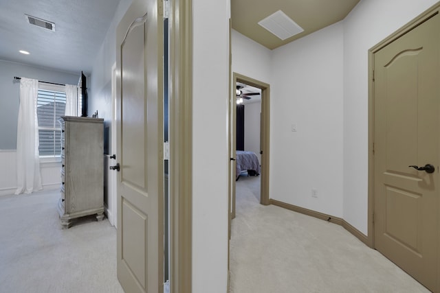 hallway with light carpet, visible vents, baseboards, and a textured ceiling