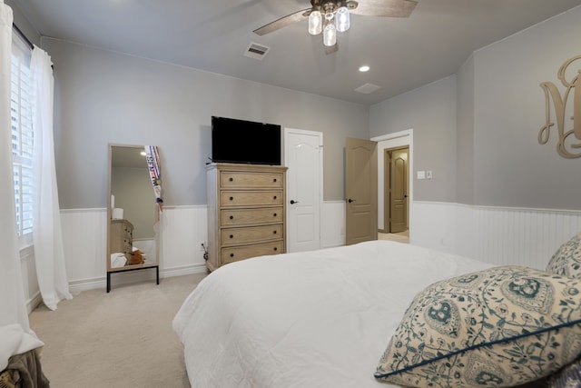 bedroom featuring ceiling fan, wainscoting, visible vents, and light colored carpet