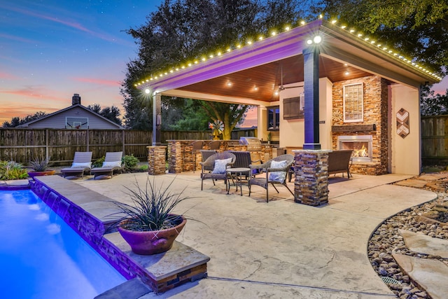 17715 Lakeside Haven Dr, Cypress, TX 77433 - patio terrace at dusk featuring an outdoor stone fireplace, exterior kitchen, and a fenced backyard