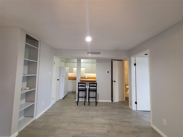 kitchen with a breakfast bar area, butcher block counters, white refrigerator, light hardwood / wood-style floors, and white cabinets