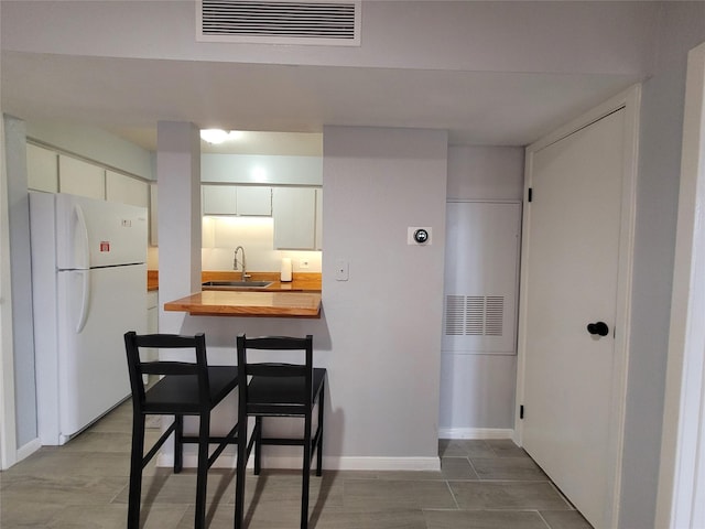 kitchen with butcher block counters, sink, white cabinetry, and white refrigerator