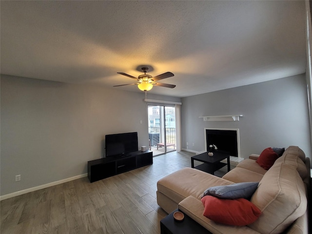 living room with ceiling fan, a textured ceiling, and light wood-type flooring