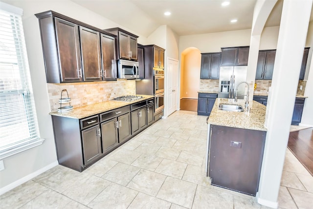 kitchen featuring dark brown cabinetry, sink, tasteful backsplash, appliances with stainless steel finishes, and light stone countertops