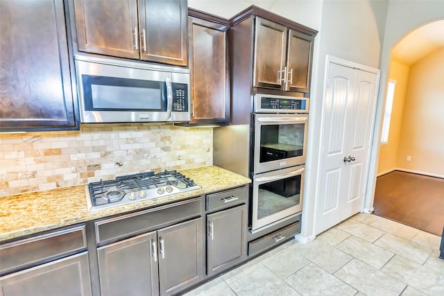 kitchen with light stone counters, dark brown cabinetry, stainless steel appliances, and decorative backsplash