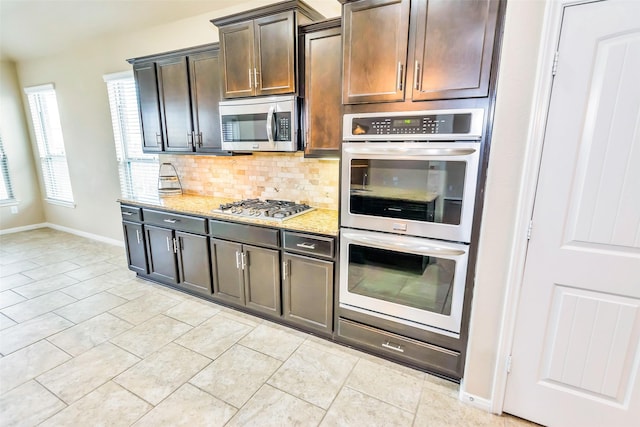 kitchen with appliances with stainless steel finishes, decorative backsplash, light tile patterned floors, light stone counters, and dark brown cabinets