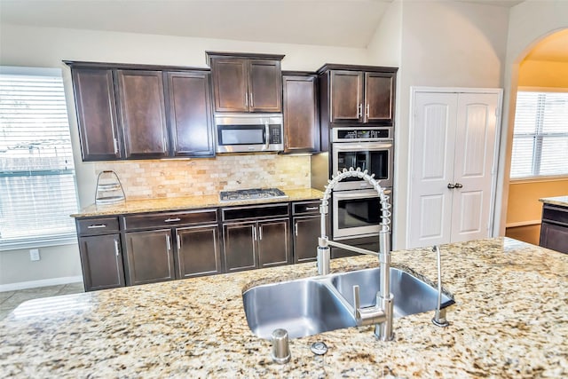 kitchen featuring sink, tasteful backsplash, light stone counters, dark brown cabinets, and stainless steel appliances