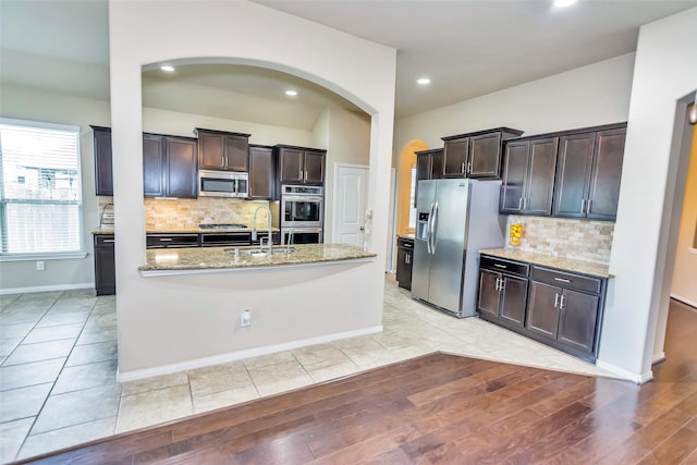 kitchen featuring light stone counters, dark brown cabinetry, appliances with stainless steel finishes, and sink