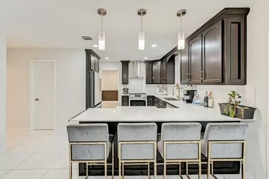 kitchen with dark brown cabinetry, sink, kitchen peninsula, stainless steel stove, and pendant lighting