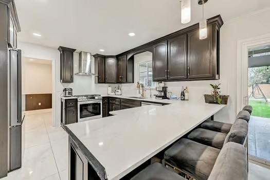 kitchen featuring wall chimney exhaust hood, sink, hanging light fixtures, kitchen peninsula, and stainless steel appliances