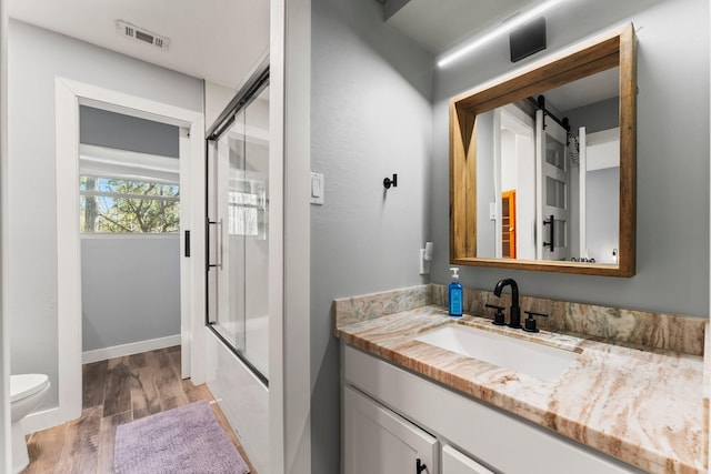 full bathroom featuring vanity, wood-type flooring, toilet, and combined bath / shower with glass door