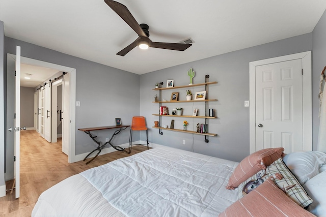 bedroom with light hardwood / wood-style floors, a barn door, and ceiling fan