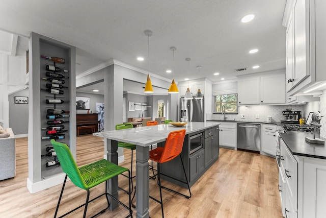 kitchen with pendant lighting, a breakfast bar, appliances with stainless steel finishes, white cabinetry, and a kitchen island