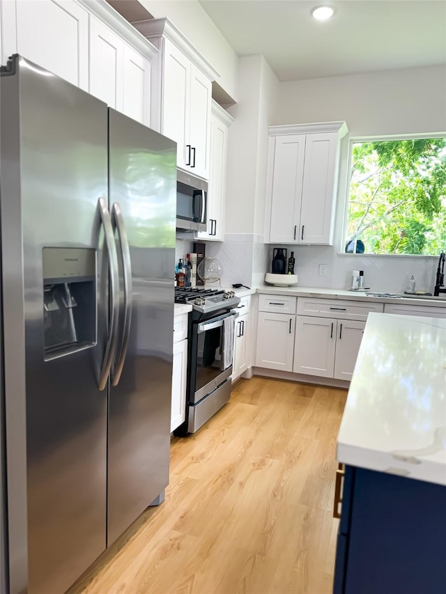 kitchen with light wood-type flooring, light countertops, decorative backsplash, appliances with stainless steel finishes, and white cabinets