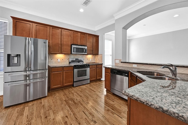 kitchen featuring sink, light hardwood / wood-style flooring, appliances with stainless steel finishes, decorative backsplash, and dark stone counters