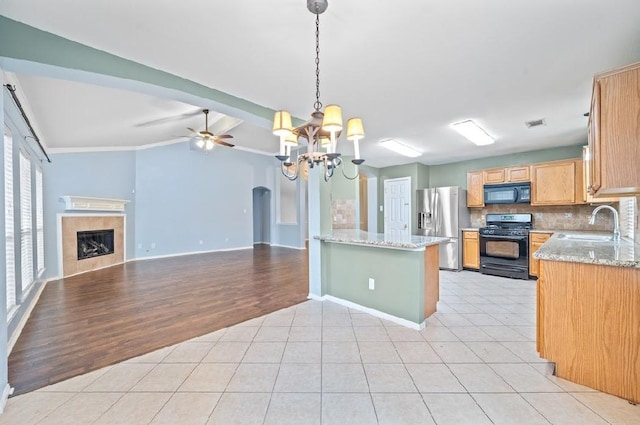 kitchen featuring sink, backsplash, a tiled fireplace, light stone counters, and black appliances