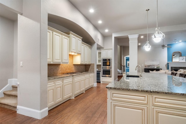 kitchen with sink, light stone counters, hanging light fixtures, stainless steel appliances, and cream cabinets