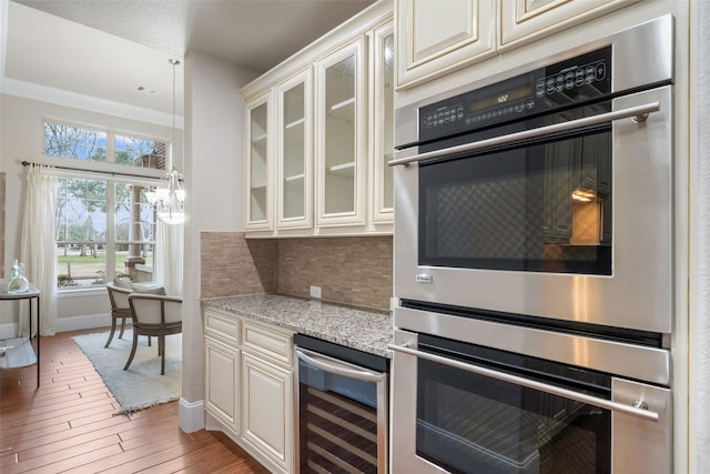 kitchen with wood-type flooring, wine cooler, decorative backsplash, light stone countertops, and stainless steel double oven