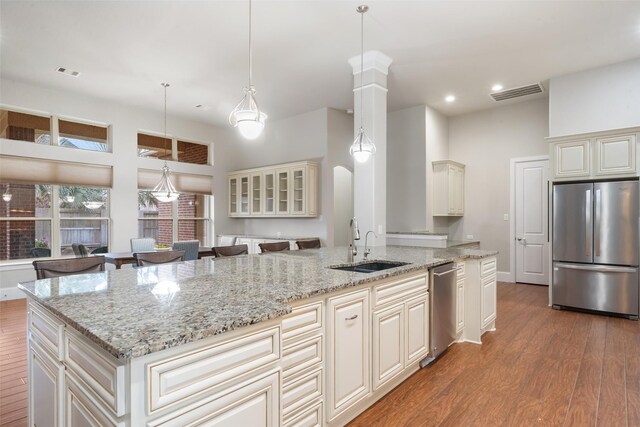 kitchen featuring pendant lighting, stainless steel appliances, a center island, cream cabinets, and light stone countertops