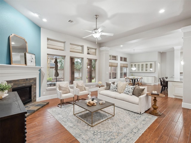 living room with decorative columns, baseboards, visible vents, wood finished floors, and a fireplace