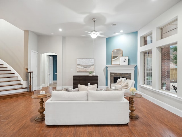 living area with arched walkways, a fireplace, recessed lighting, wood finished floors, and stairs