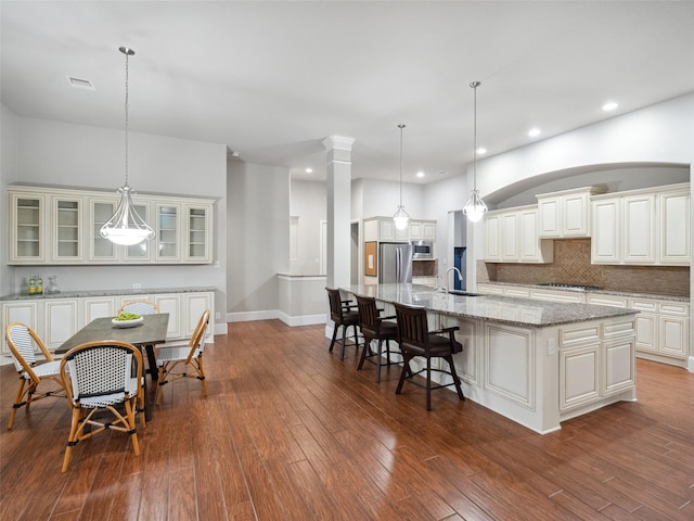 kitchen featuring pendant lighting, a large island, glass insert cabinets, appliances with stainless steel finishes, and light stone countertops