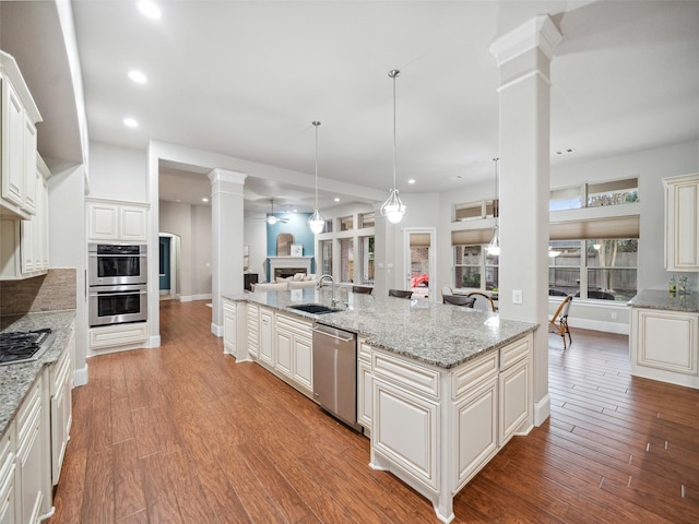 kitchen with a kitchen island with sink, stainless steel appliances, ornate columns, a fireplace, and a sink