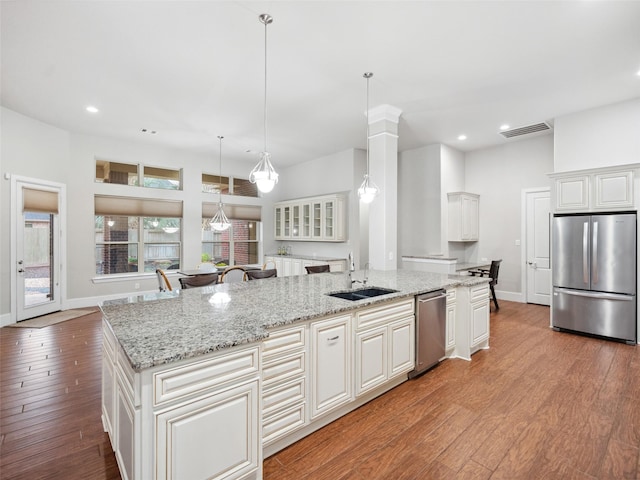 kitchen with pendant lighting, a center island with sink, stainless steel appliances, visible vents, and a sink