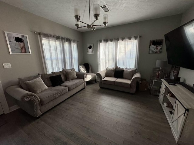 living room featuring a notable chandelier, a textured ceiling, dark wood-type flooring, and a healthy amount of sunlight