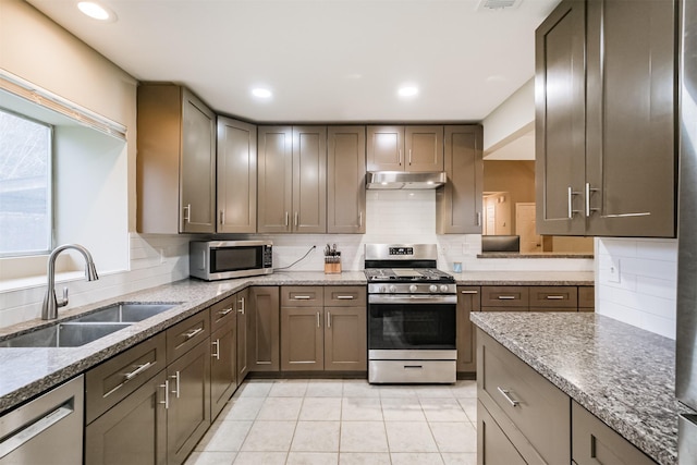 kitchen with appliances with stainless steel finishes, light stone countertops, sink, and backsplash