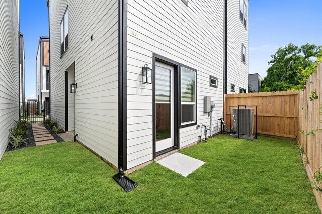 rear view of property with central AC, a fenced backyard, and a yard
