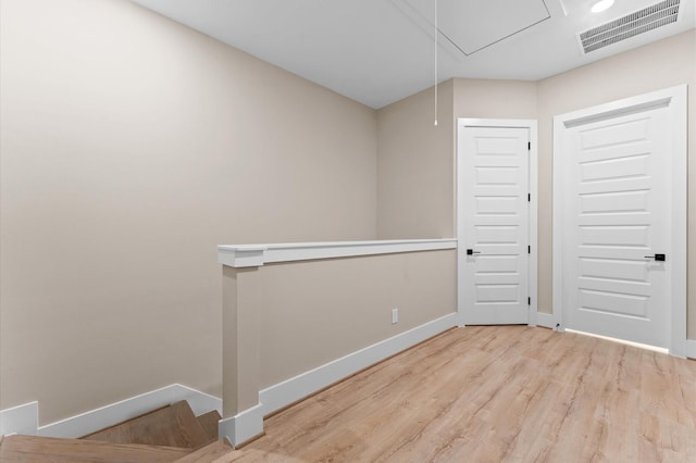 spare room with attic access, visible vents, wood finished floors, and baseboards