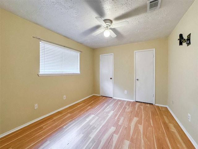 unfurnished bedroom with ceiling fan, multiple closets, light hardwood / wood-style floors, and a textured ceiling