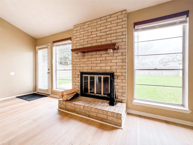 unfurnished living room with a brick fireplace, baseboards, a wealth of natural light, and wood finished floors