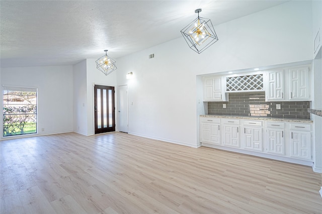 unfurnished living room featuring a textured ceiling, high vaulted ceiling, a chandelier, and light wood-type flooring