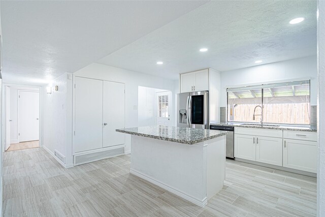 kitchen featuring sink, appliances with stainless steel finishes, light stone counters, white cabinets, and a kitchen island