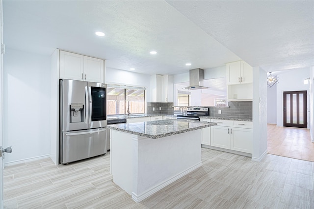 kitchen with light stone counters, white cabinets, appliances with stainless steel finishes, and island range hood