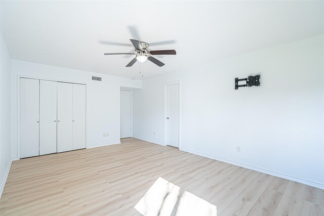 unfurnished bedroom featuring ceiling fan, light wood-type flooring, and two closets