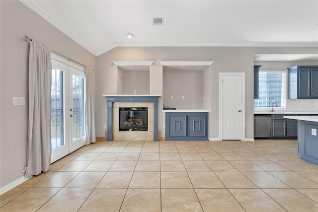 unfurnished living room with a tiled fireplace, light tile patterned floors, crown molding, and french doors