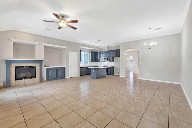 unfurnished living room with a tiled fireplace, ornamental molding, ceiling fan with notable chandelier, and light tile patterned floors