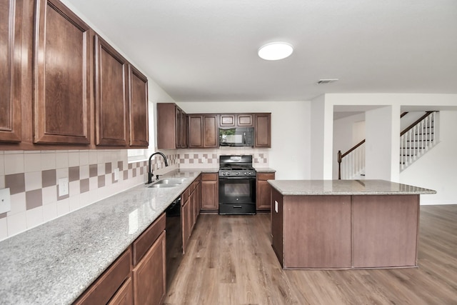 kitchen featuring sink, light stone counters, black appliances, light hardwood / wood-style floors, and decorative backsplash